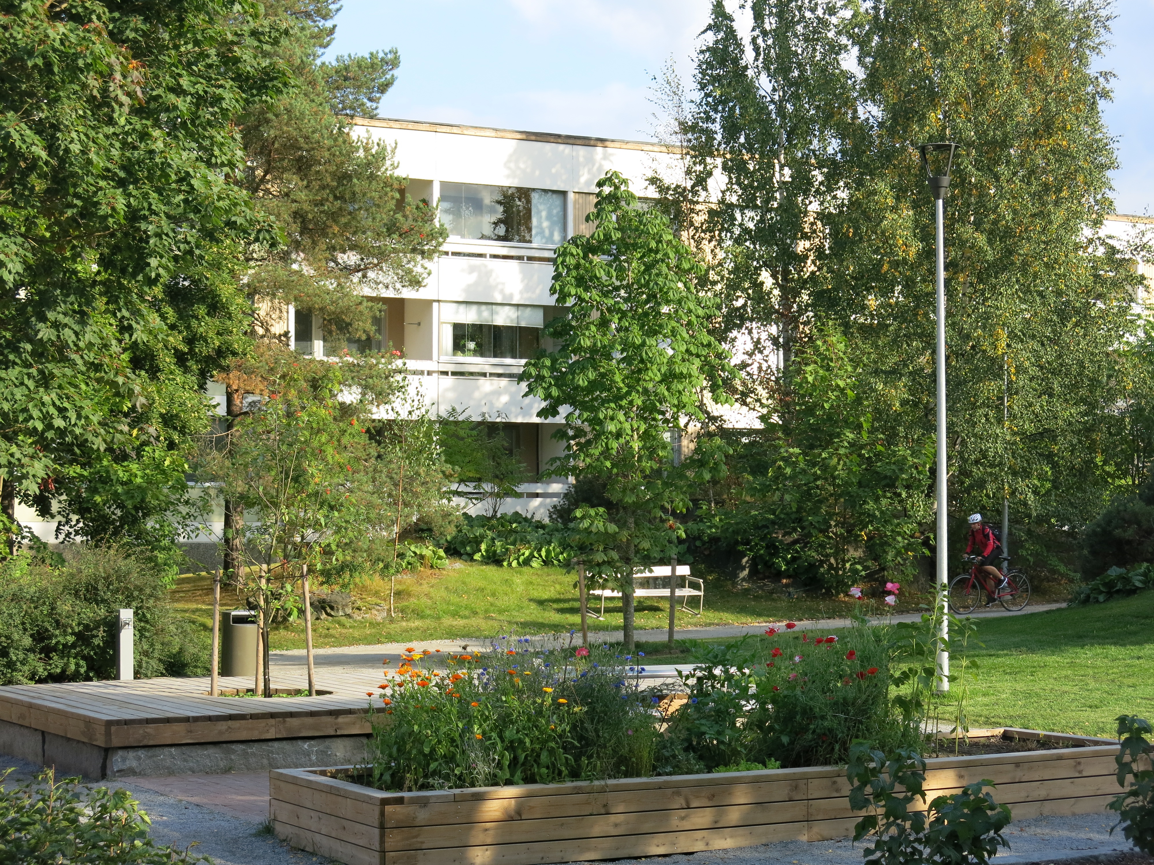 Puiston rakenteita ja istutuksia, taustalla matala 3-kerroksinen kerrostalo.