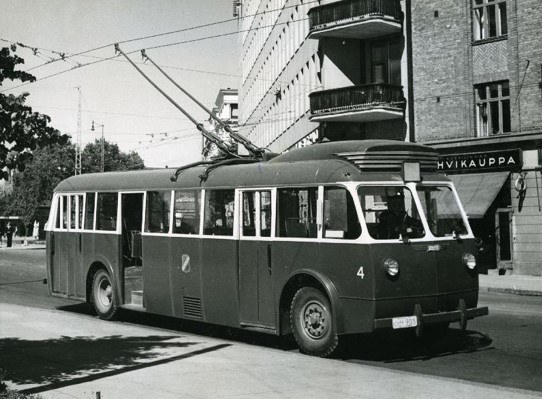 Kuva johdinautosta, jonka katolta ajojohtimet ottavat virtaa kadun yläpuolella olevista sähköjohdoista. Taustalla on kerrostaloja.