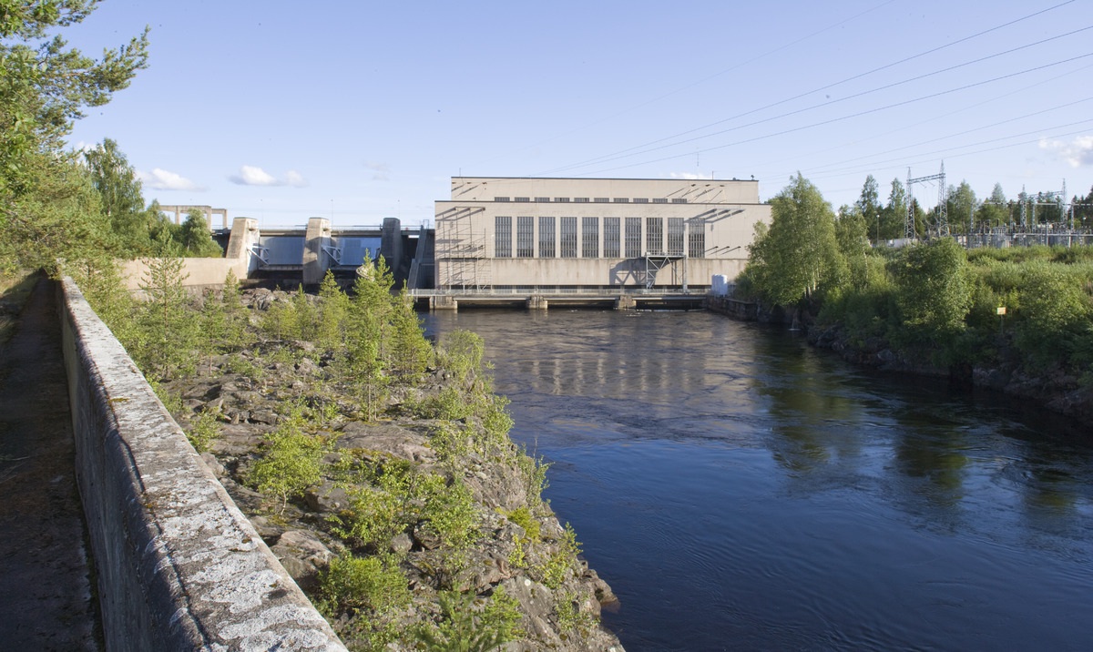 Yleiskuva voimalaitoksesta. Etualalla alakanavaa ja kallioista rantaa. Voimalaitoksen patorakenteet, voimalaitosrakennus ja muuntajakenttä kuvan taka-alalla.